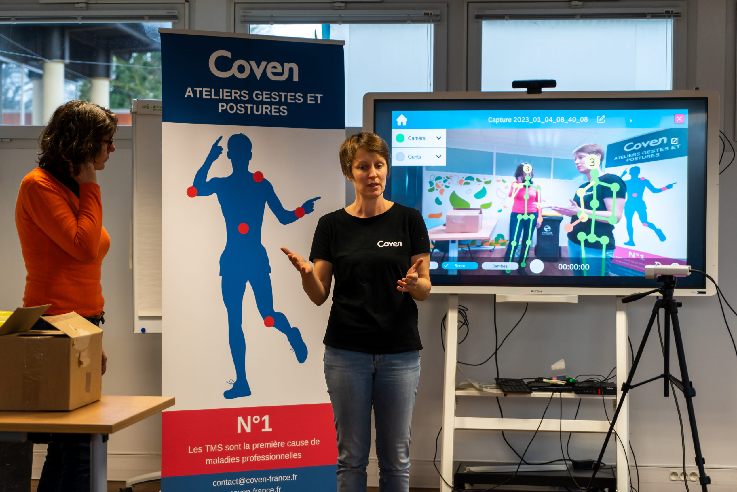 Photo d'une animatrice Coven en train de faire une démonstration de l'atelier prévention des TMS avec une caméra qui permet de mettre en lumière les contraintes posturales des participants.
