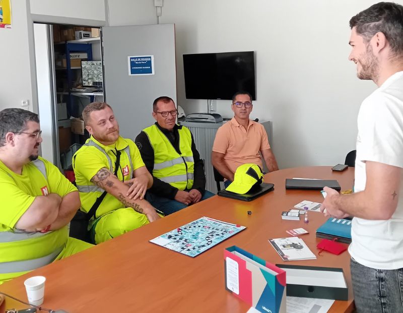 Des salariés du groupe Nicollin assis autour d'une table qui jouent à la Box Prévention Nicollin conçue par Coven